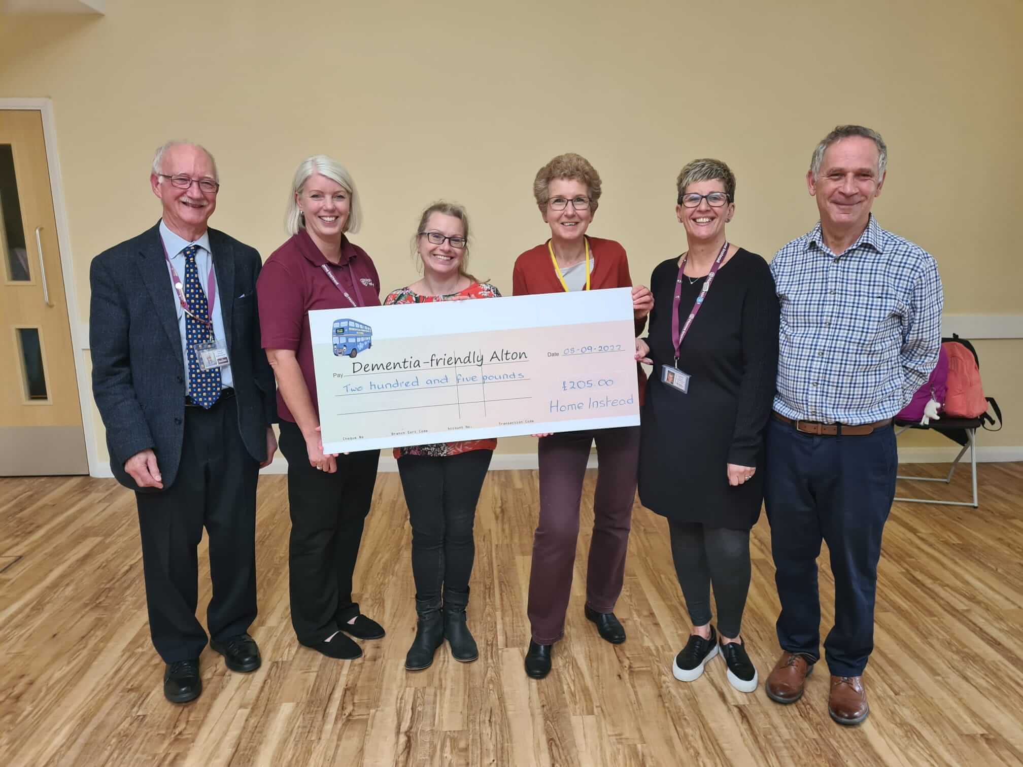 Six people holding a large ceremonial check for 1205 pounds from Home Instead to Dementia-friendly Alton. - Home Instead