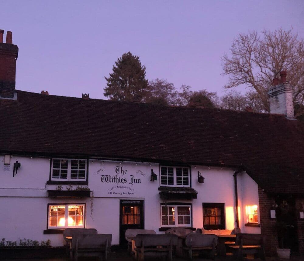 A quaint, illuminated inn with a wooden sign, benches outside, and a dusky sky in the background. - Home Instead