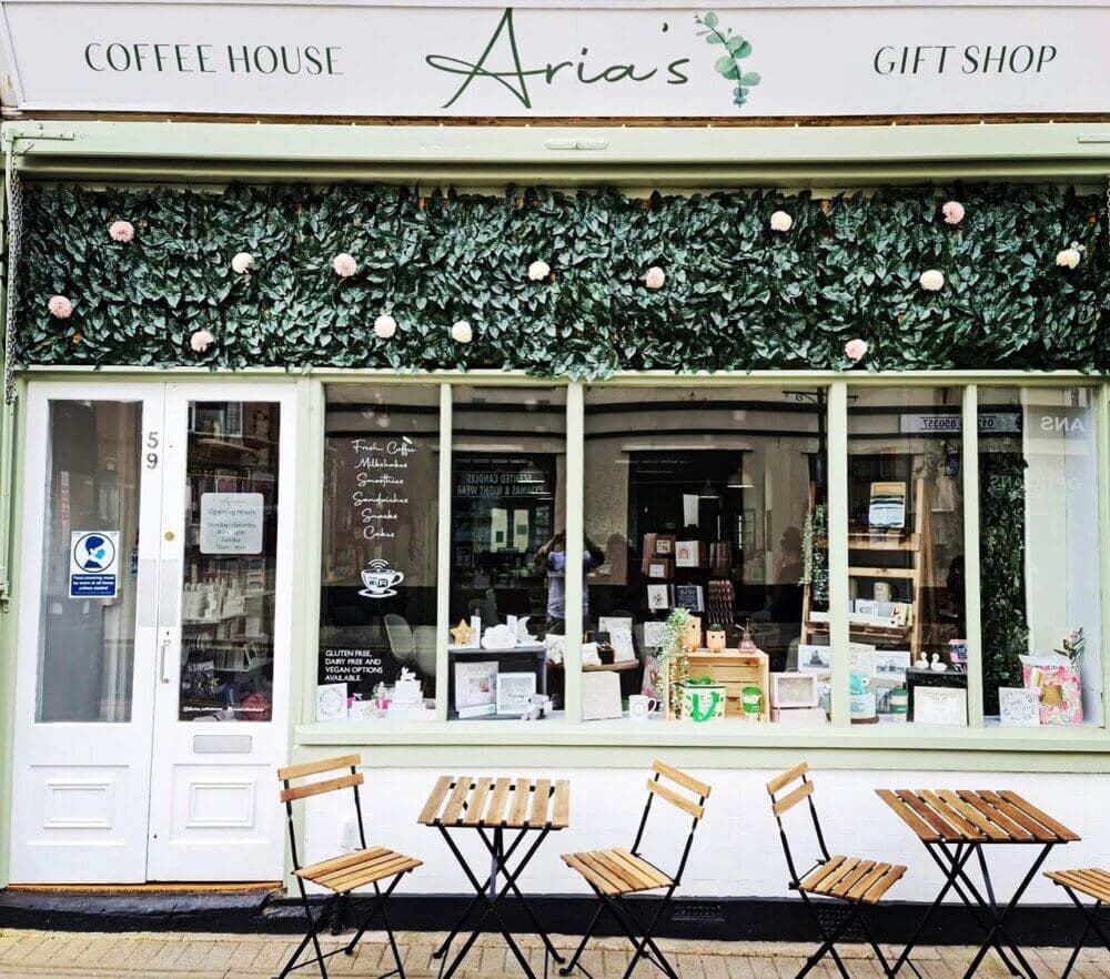 Exterior of Aria's, a coffee house and gift shop, with outdoor seating and a floral display above the windows. - Home Instead