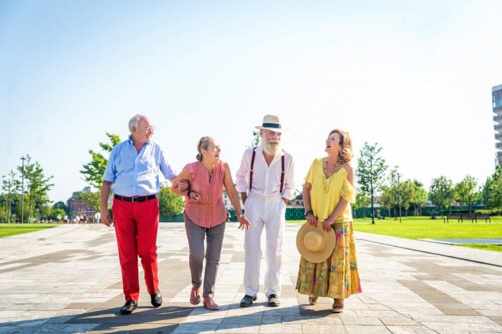 Four elderly people walking together outdoors, smiling and enjoying a sunny day in a park. - Home Instead
