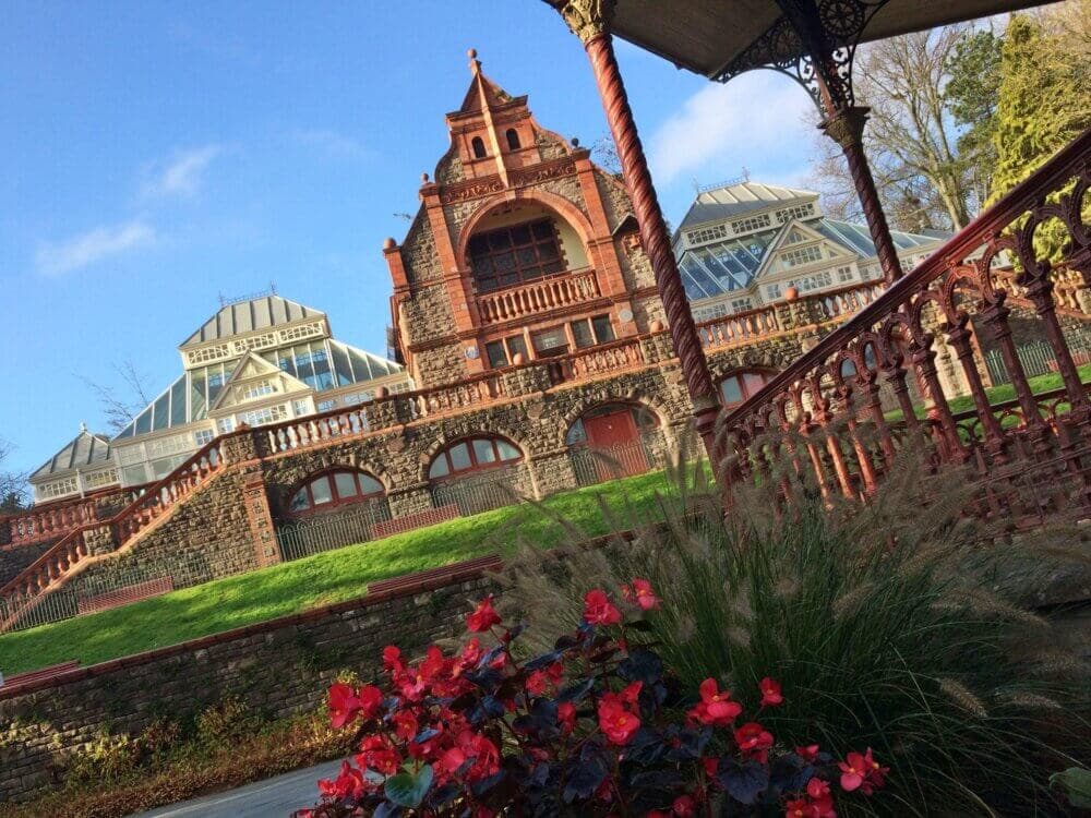 Historic mansion with Victorian architecture, ornate red brickwork, green lawn, and vibrant red flowers in the foreground. - Home Instead
