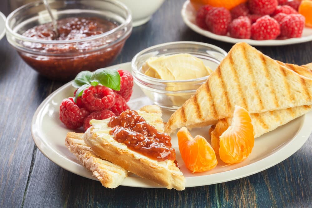 Plate with toast, butter, jam, raspberries, and orange slices; more jam and raspberries in bowls in the background. - Home Instead