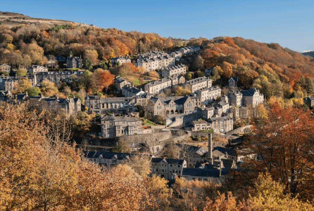 Hillside village with autumn-colored trees, featuring stone houses and a clear blue sky in the background. - Home Instead
