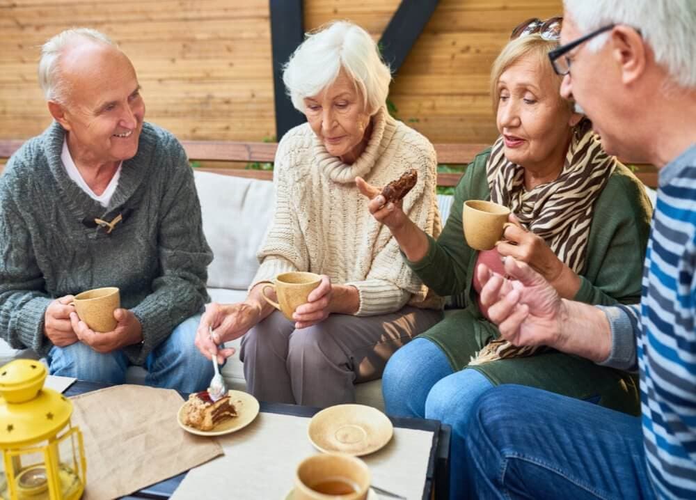 Four elderly people enjoying tea and cake together while seated outside on a cosy patio. - Home Instead Southampton