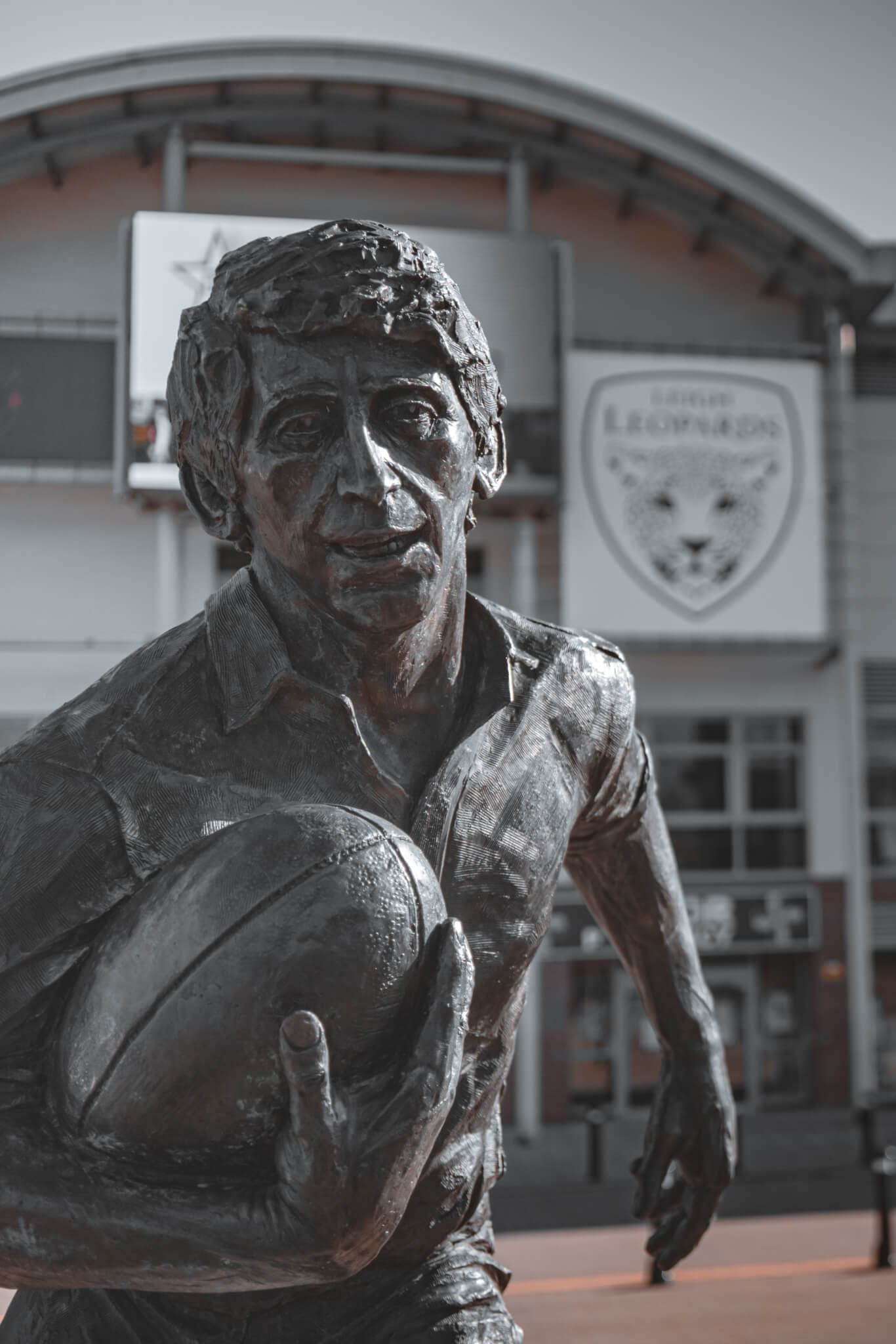 A bronze statue of a rugby player holding a ball is located in front of a building with a "Tigers Legends" sign. - Home Instead
