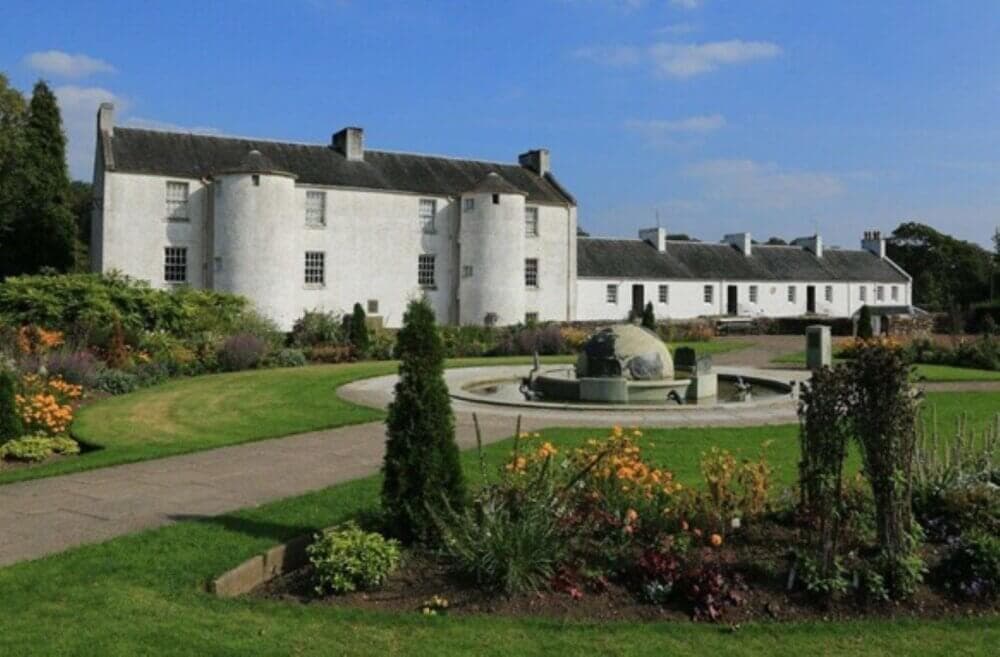 A large white historic building with round towers, a central fountain, and a landscaped garden under a blue sky. - Home Instead
