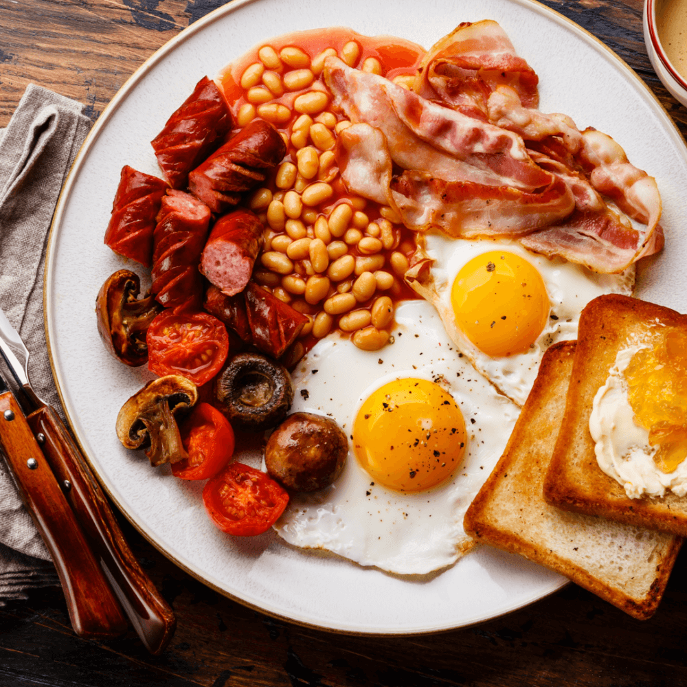 A hearty breakfast plate with fried eggs, bacon, sausages, baked beans, mushrooms, tomatoes, and toast with jam. - Home Instead