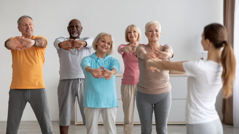 A group of seniors doing stretching exercises in a fitness class, led by an instructor. - Home Instead