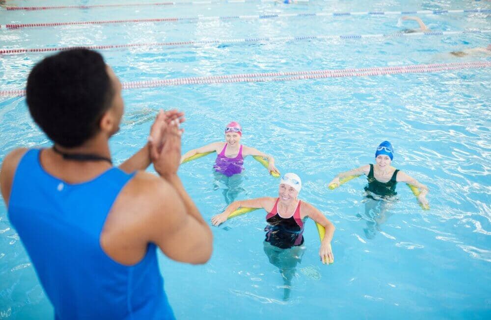 Instructor applauding three swimmers in a pool, all wearing swim caps and goggles, practicing in designated lanes. - Home Instead