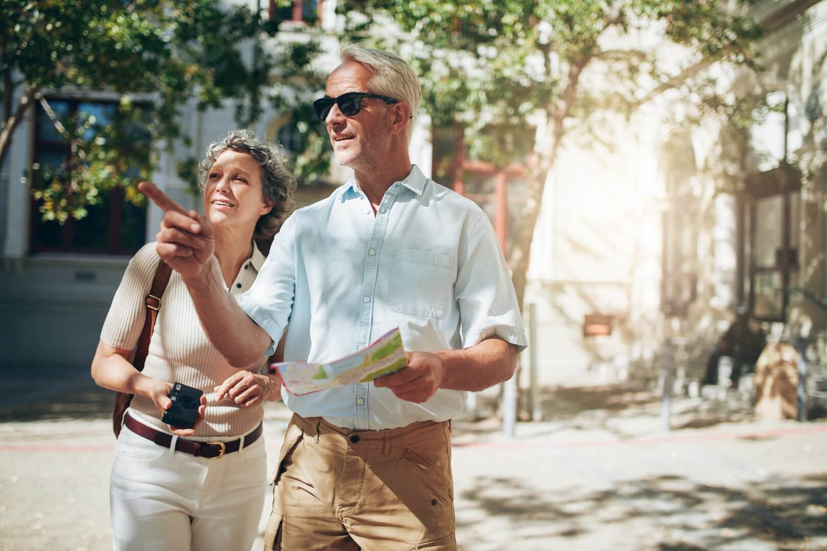An elderly man and woman outdoors, the man holding a map and pointing while the woman smiles. - Home Instead