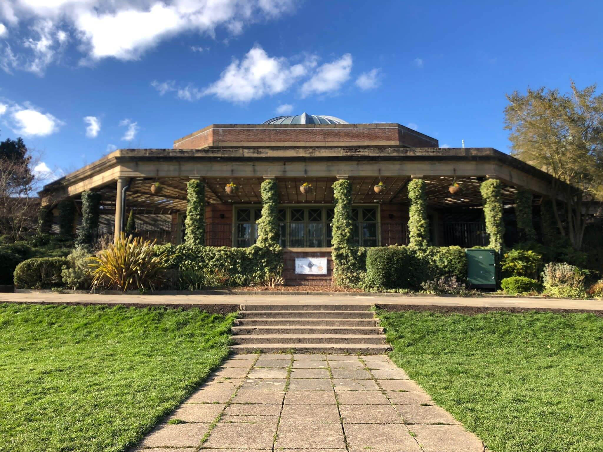 A scenic view of a park pavilion with ivy-covered columns under a clear, blue sky. Steps lead up to the pavilion. - Home Instead