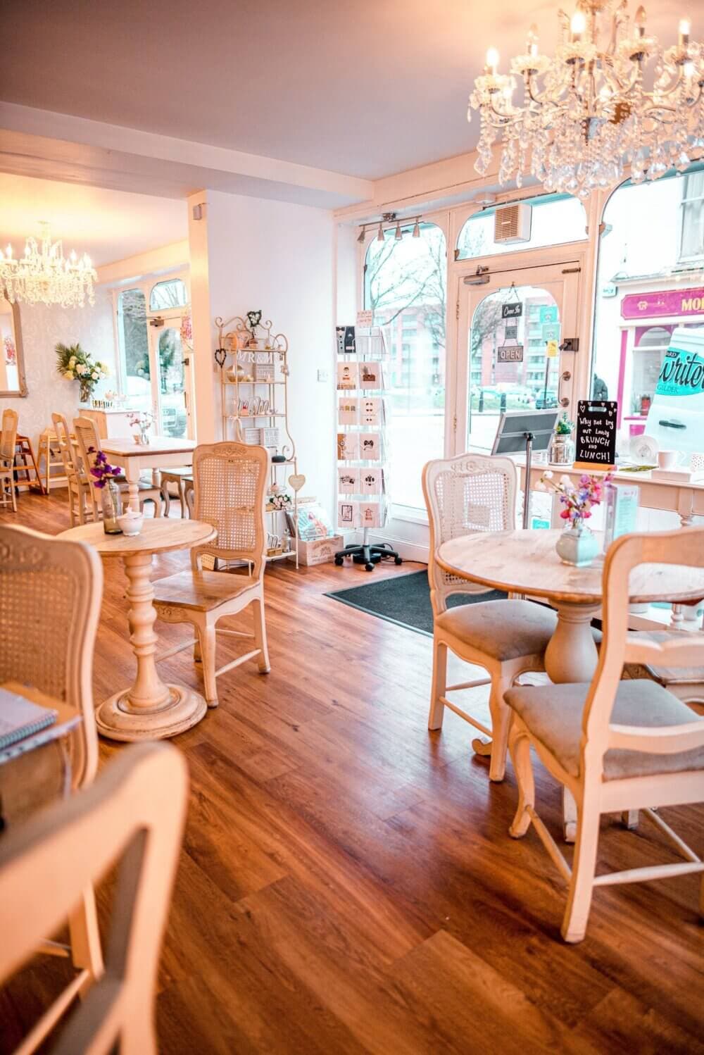 Cozy café interior with wooden tables and chairs, decorative chandeliers, and a display rack by the entrance. - Home Instead