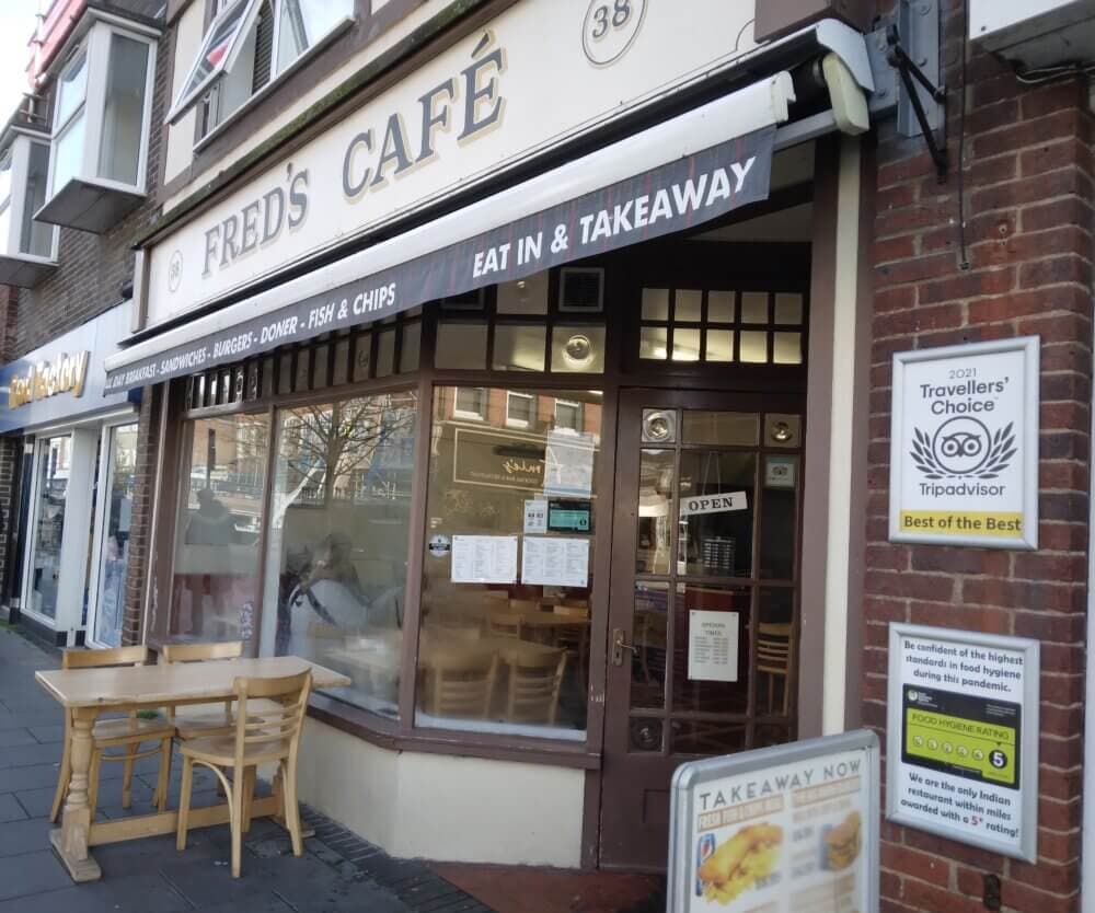 Street view of "Fred's Café" with outdoor seating and signs showcasing TripAdvisor's 2021 Traveler's Choice award. - Home Instead