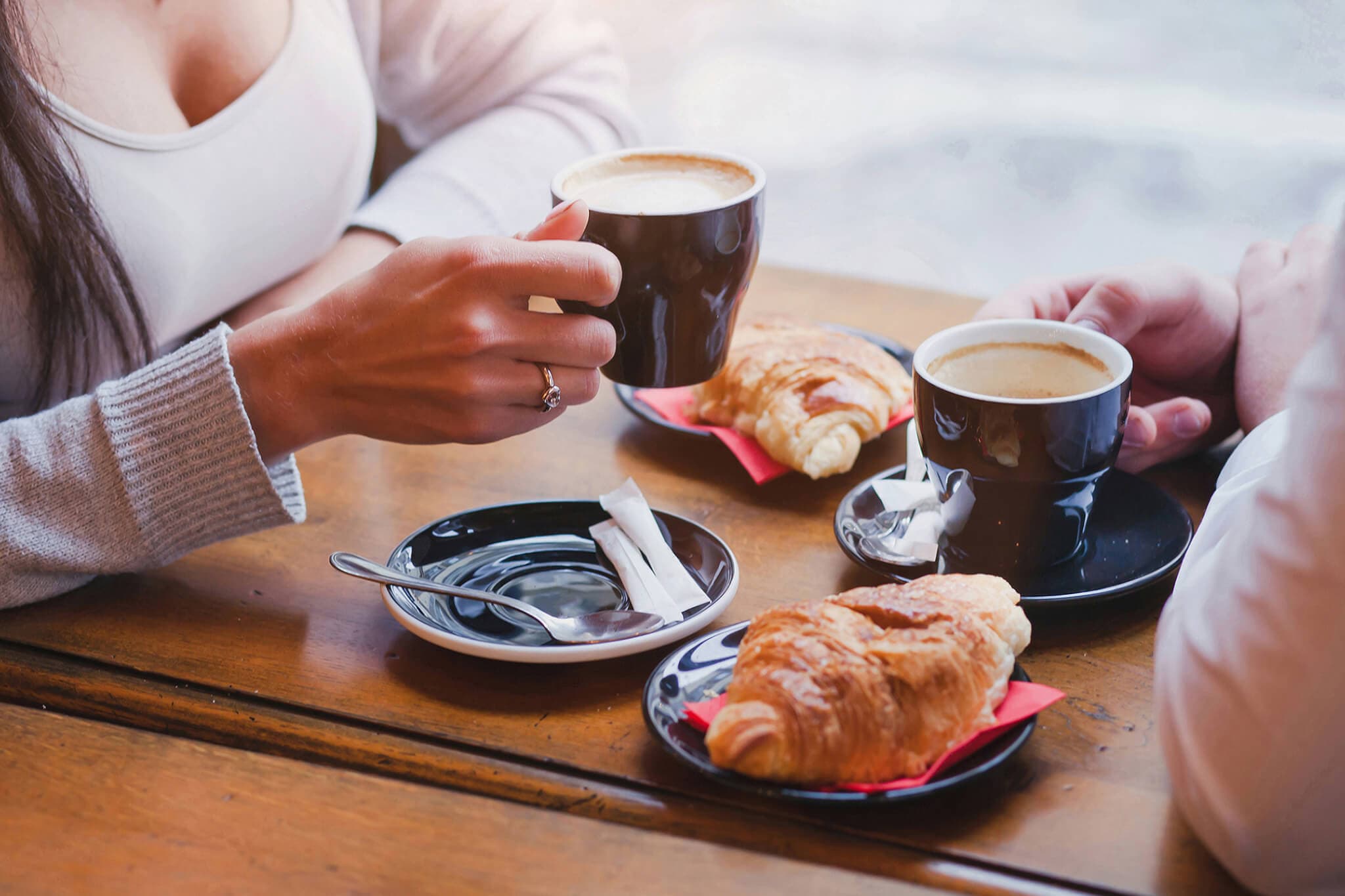 Two people having coffee and croissants at a wooden table, with hands visible holding cups. - Home Instead