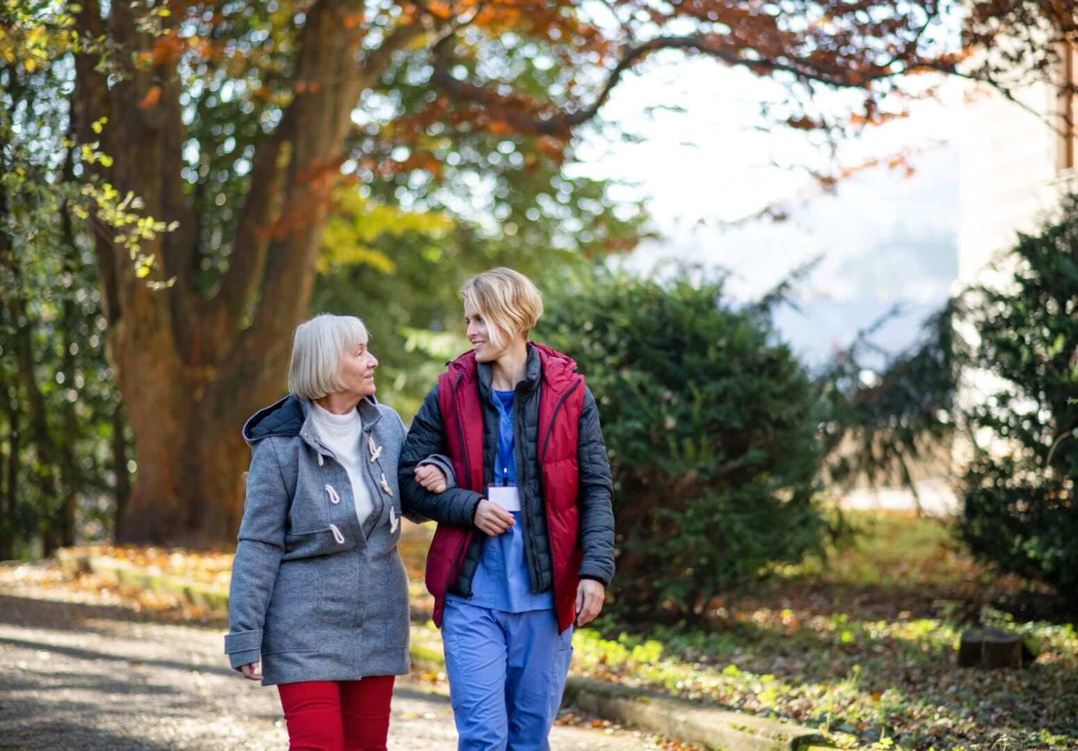 Older woman and Care Professionals walking outside in the fall, surrounded by trees with colourful leaves. - Home Instead Southampton