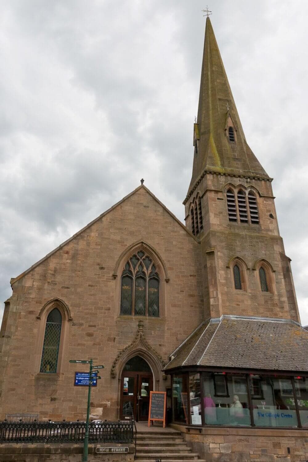 A historic church with a tall spire, arched windows, and a small entrance on an overcast day. - Home Instead