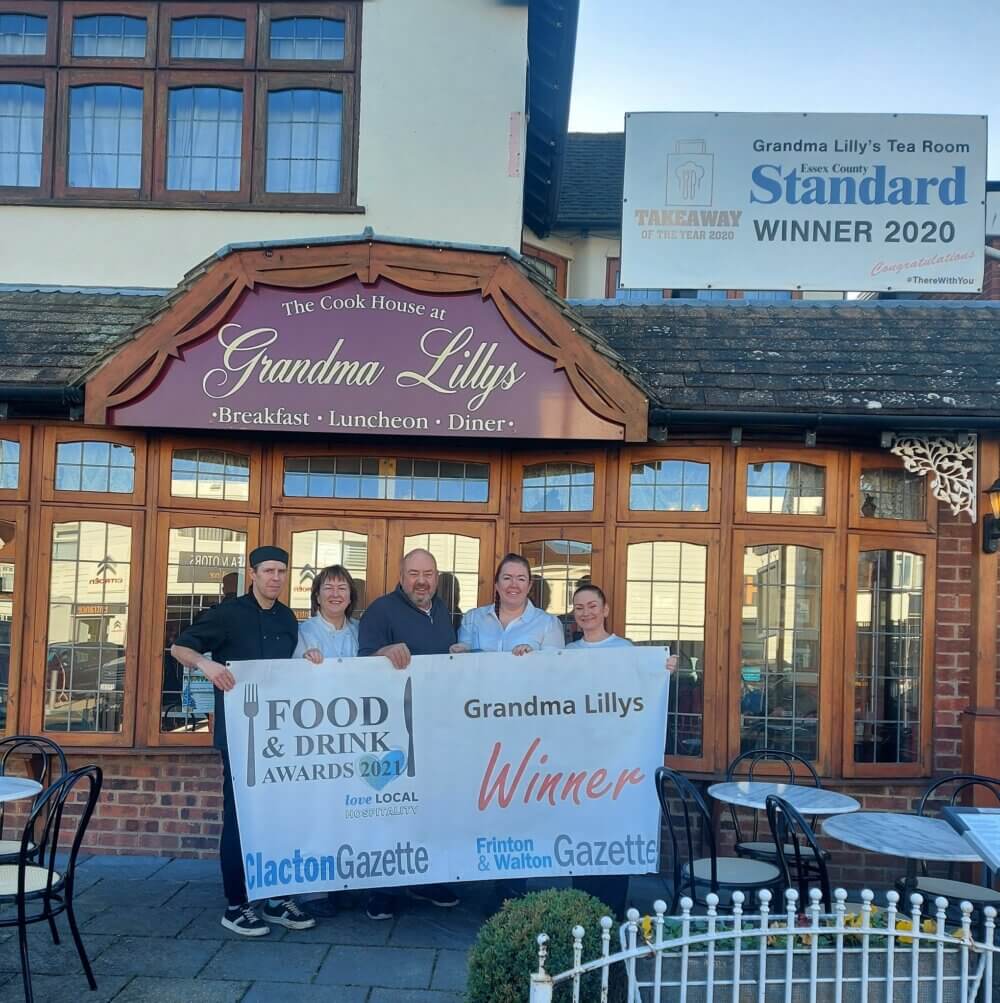 Five people holding award banners in front of Grandma Lilly's Tea Room, which has won the Food & Drink Awards 2021. - Home Instead