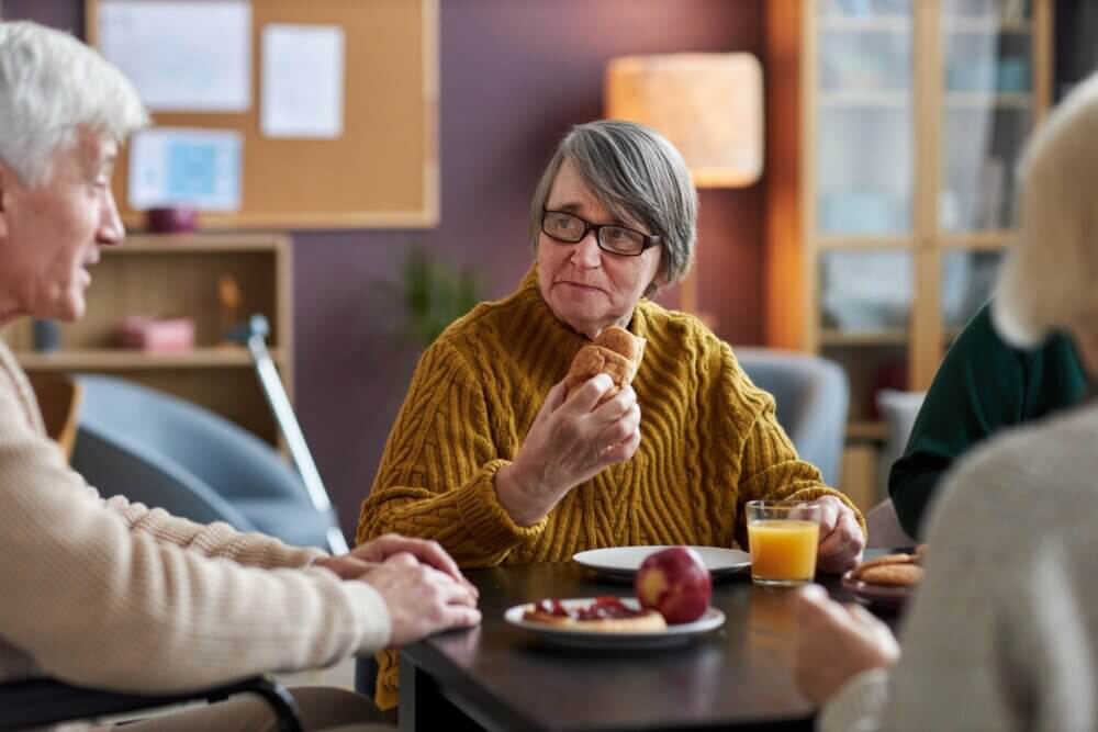 Three elderly people sitting around a table, sharing a meal and conversing with each other. - Home Instead