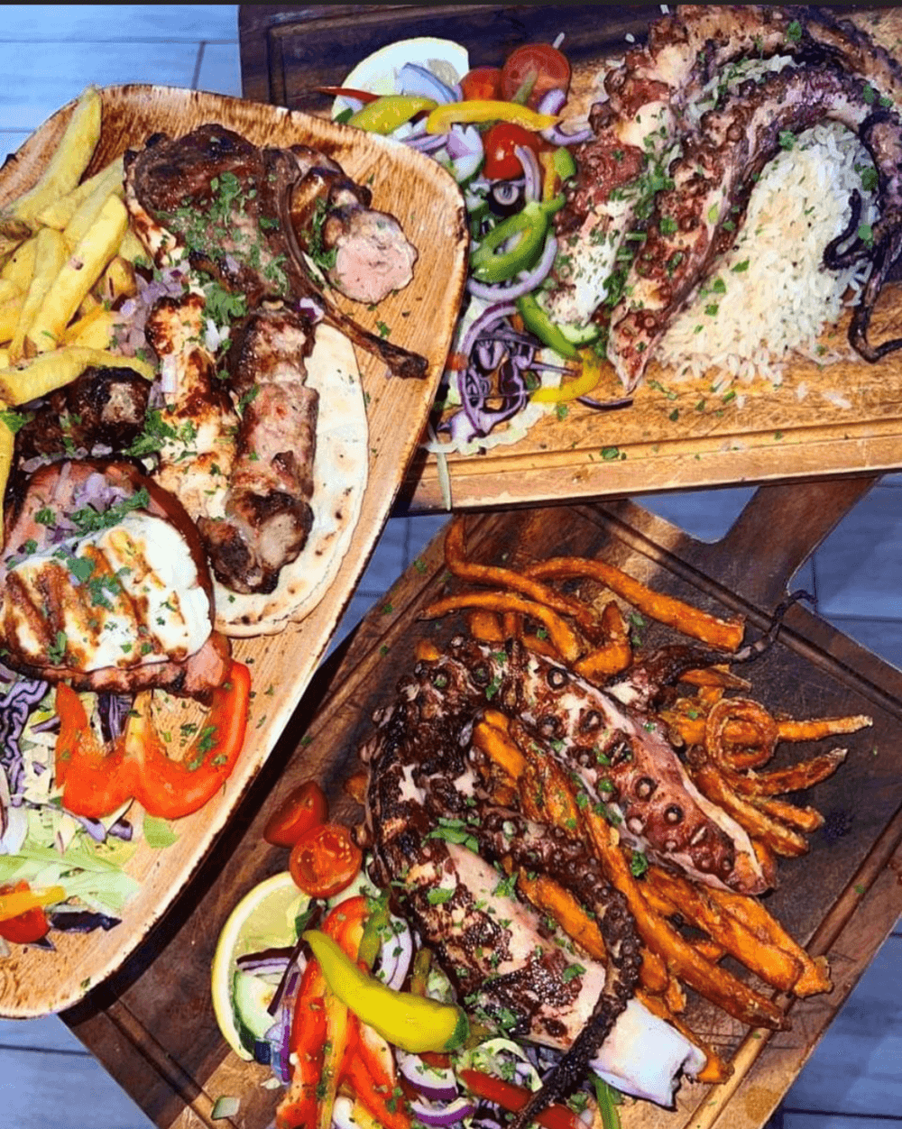 Plates of grilled octopus, skewers, fries, and vegetables on wooden boards. - Home Instead