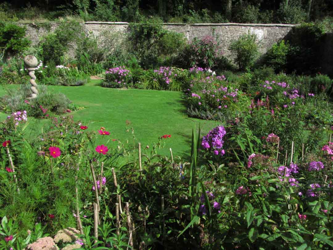 A lush garden with vibrant flowers, a manicured lawn, and a stone wall in the background. - Home Instead