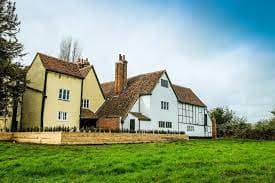 A large, traditional countryside house with white and yellow walls, red-tiled roof, and a grassy lawn in front. - Home Instead