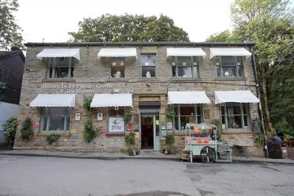 Stone building with teal awnings, labeled Hawley Tea Heritage Centre & Tea Rooms, with greenery and outdoor seating. - Home Instead