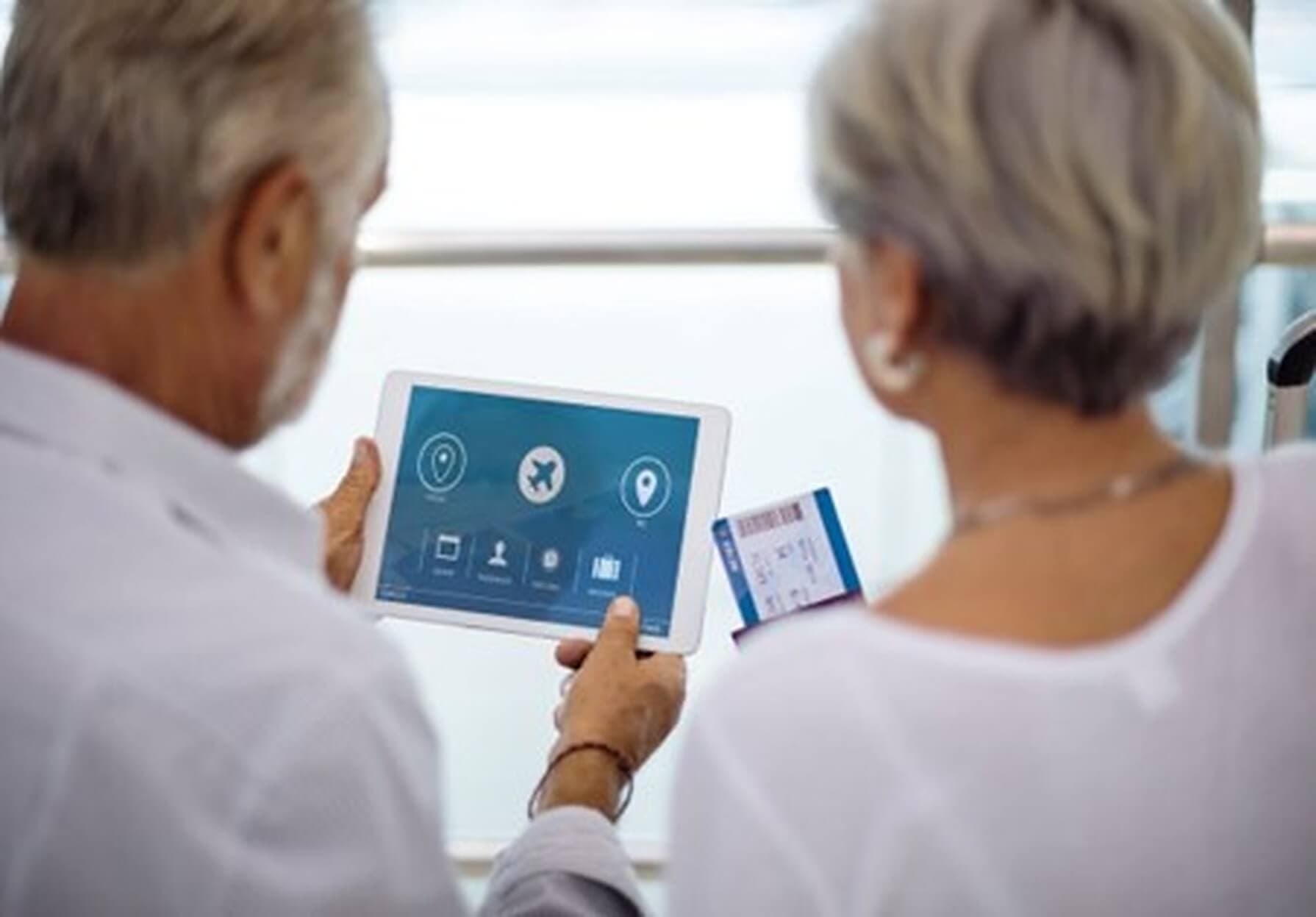 Two people looking at a travel app on a tablet, holding a set of boarding passes in an airport setting. - Home Instead