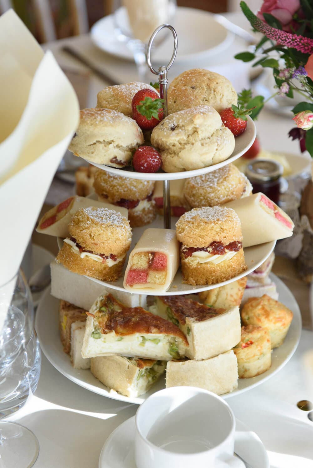 A three-tiered tray with scones, pastries, and sandwiches, accompanied by fresh strawberries and a teacup nearby. - Home Instead