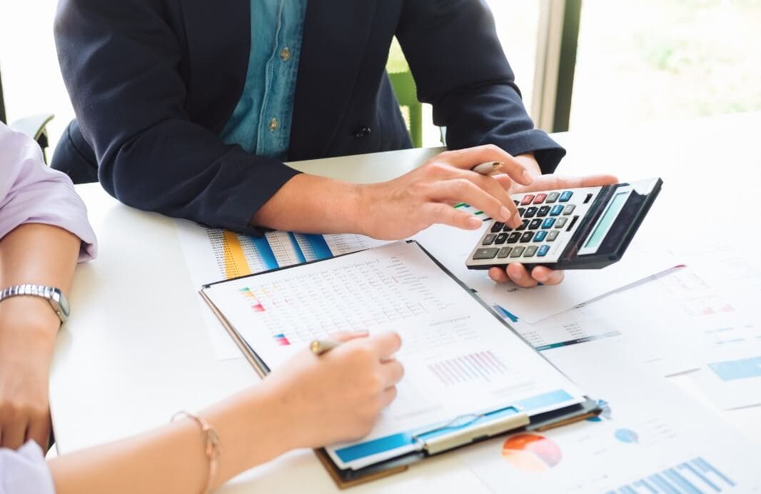 Two individuals reviewing financial documents with charts and graphs while one person uses a calculator. - Home Instead