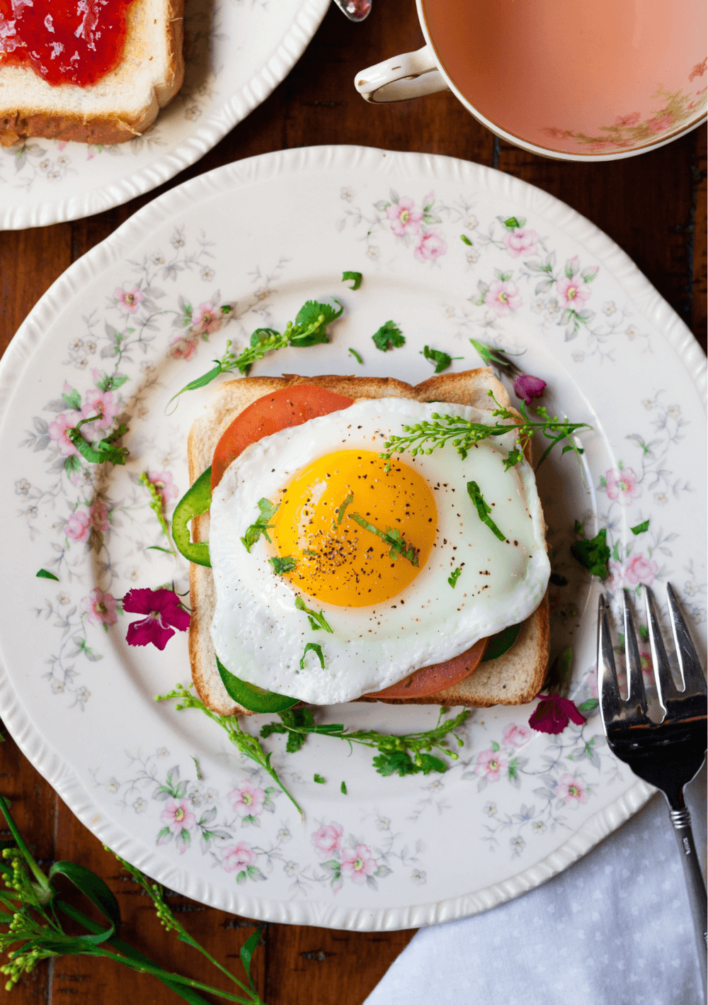 A plate with toast topped with a sunny-side-up egg, tomato, and greens, alongside a cup of tea and a fork. - Home Instead