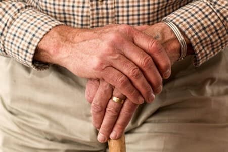 A close-up of an elderly person's hands resting on a cane, wearing a checkered shirt and a silver bracelet. - Home Instead