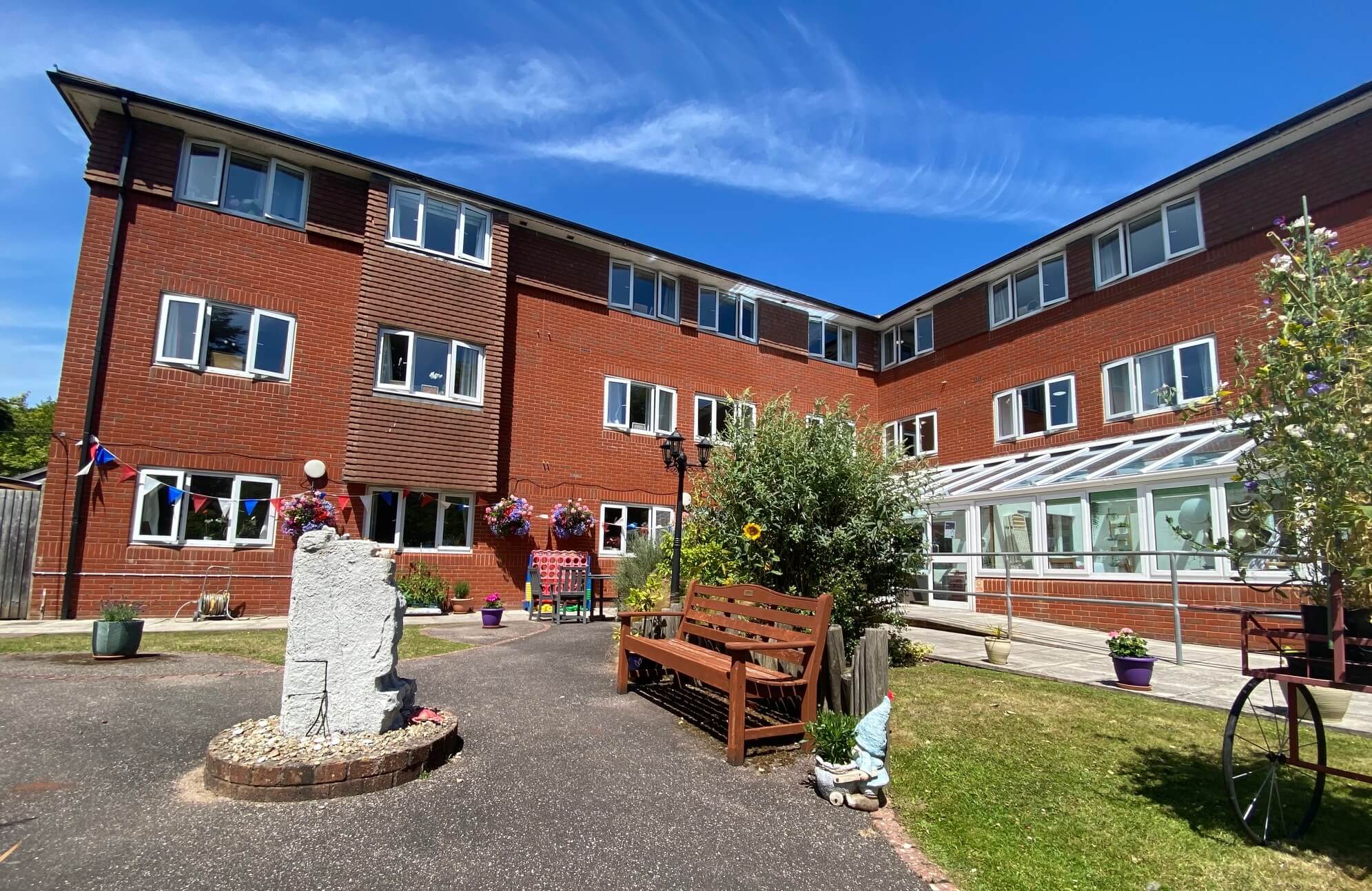 Red brick building with multiple windows, outdoor benches, plants, and a clear blue sky in the background. - Home Instead