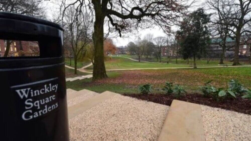 Park steps with a trash bin labeled "Winckley Square Gardens" lead to a grassy area lined with trees and pathways. - Home Instead