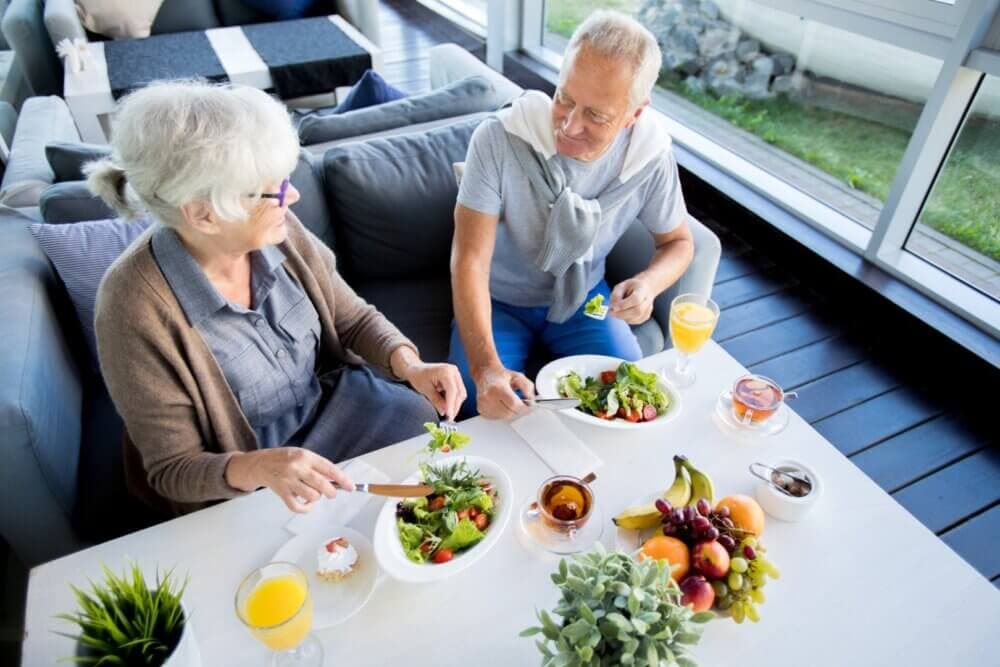 Two elderly people enjoying a healthy meal together at a bright, indoor dining space with large windows. - Home Instead Southampton