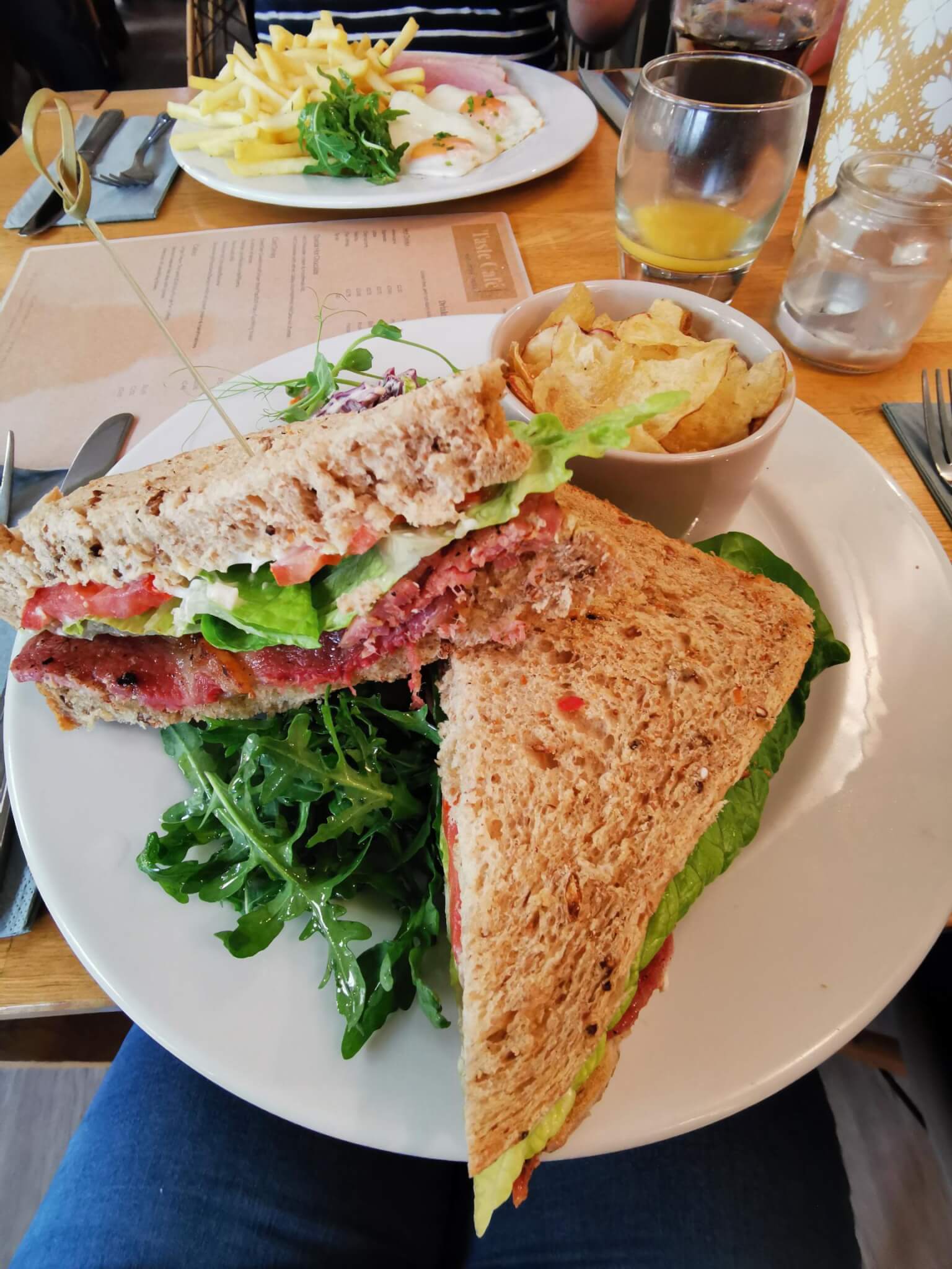 A plate with a sandwich filled with lettuce and meat, a side salad, and a bowl of potato chips on a wooden table. - Home Instead