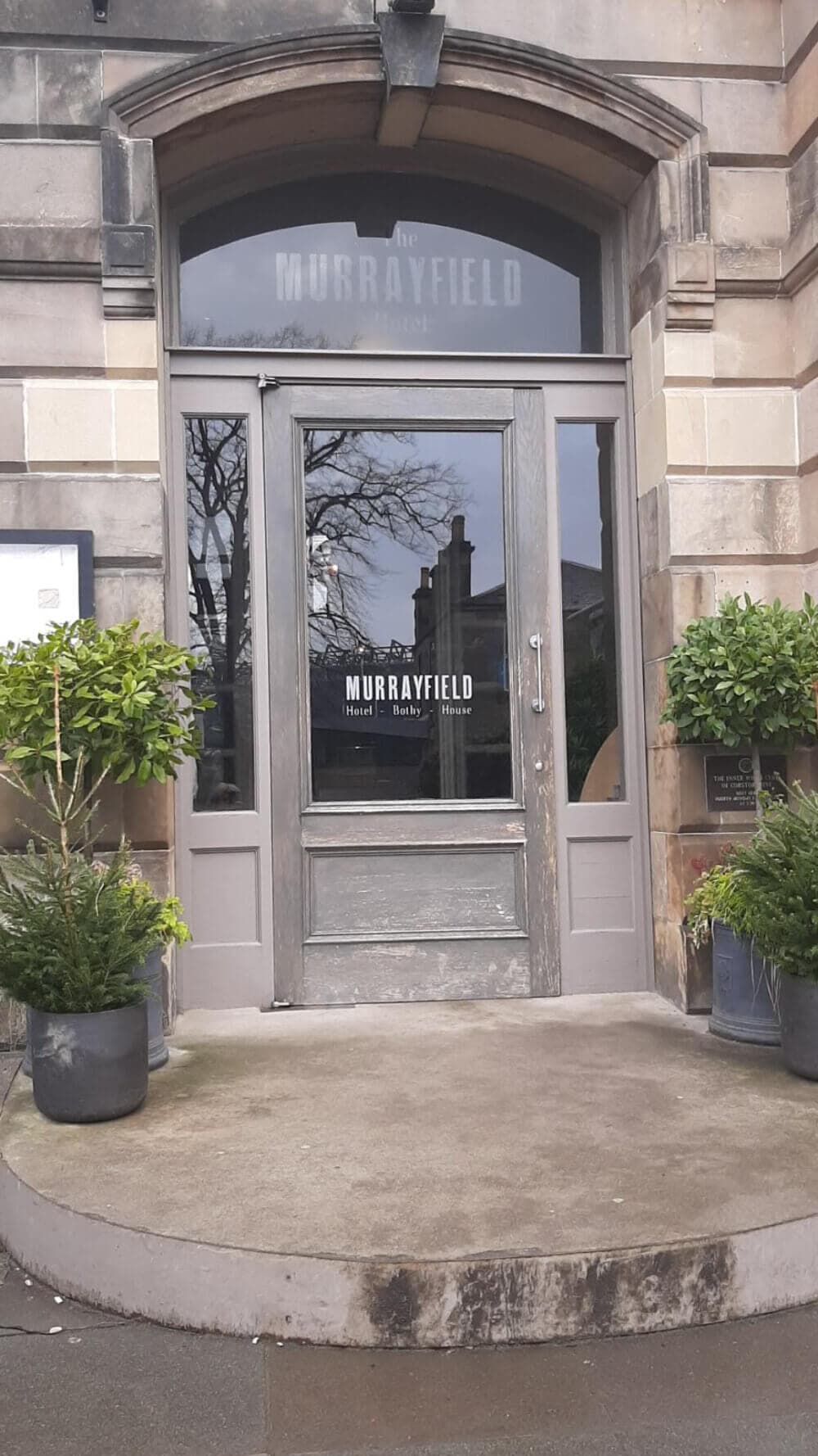 Entrance of The Murrayfield Hotel, featuring a stone archway, a glass door, and potted plants on either side. - Home Instead