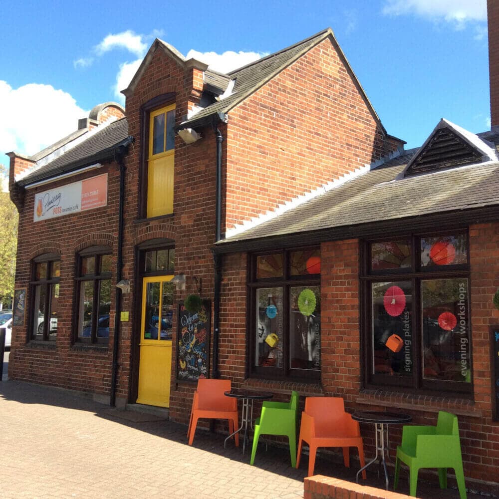 A brick building with colorful chairs outside, featuring a yellow door and large windows adorned with art. - Home Instead