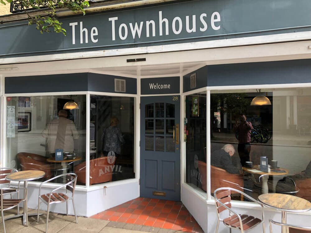 A cafe named "The Townhouse" with outdoor seating, large windows, and people inside. - Home Instead