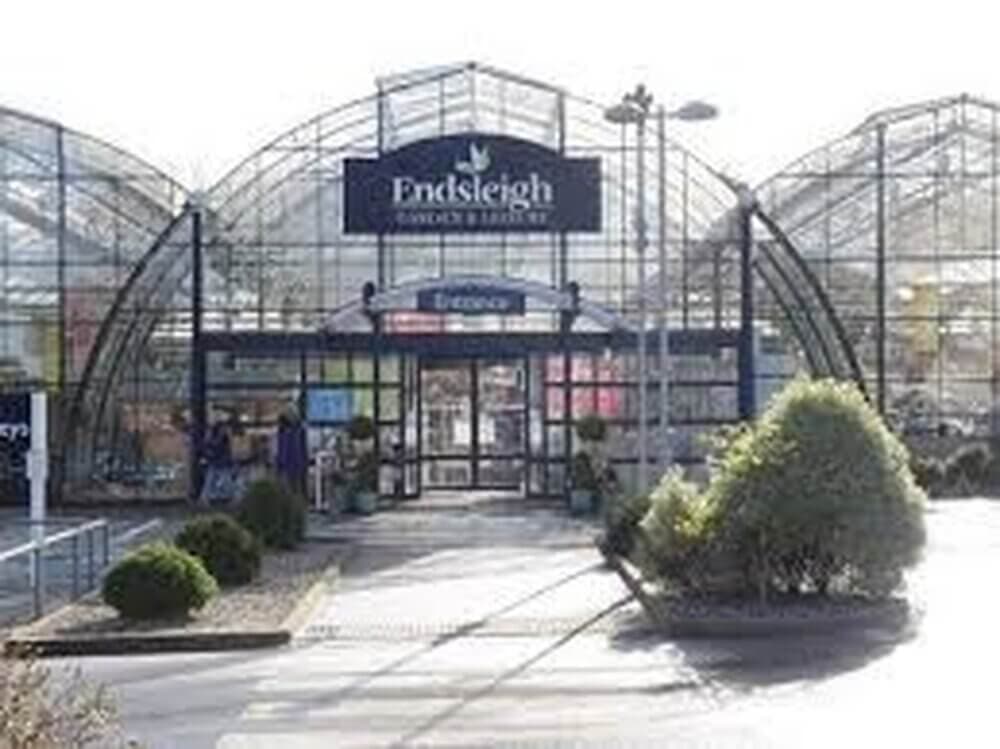 Front entrance of Endsleigh Garden Centre with glass greenhouse structures and greenery in the foreground. - Home Instead