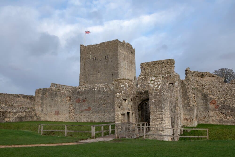 A medieval stone castle with a flag flying on top, surrounded by green grass under a cloudy sky. - Home Instead