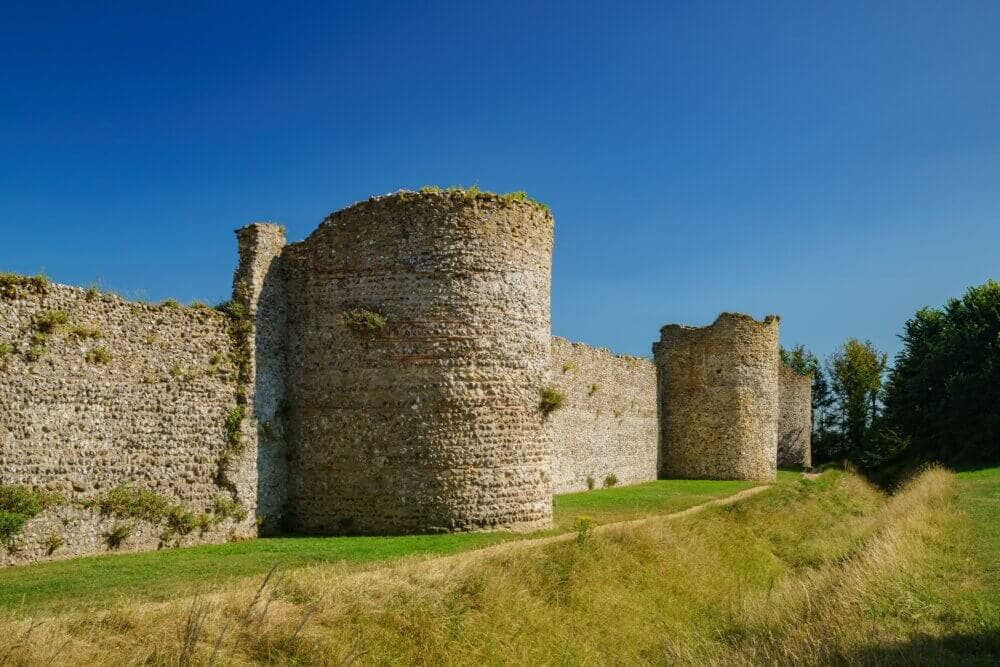 Ancient stone ruins of a castle with large round towers standing in a grassy landscape under a clear blue sky. - Home Instead