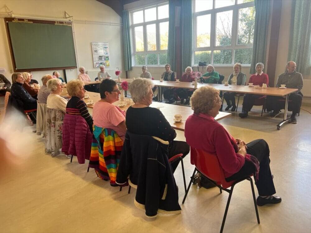 A group of elderly people sit in a circle around a large table in a well-lit community room. - Home Instead