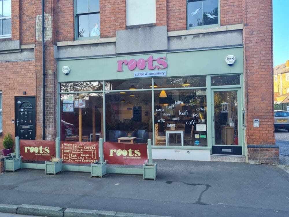 Storefront of 'Roots Coffee & Community' with outdoor seating, a sidewalk, and front window displaying words related to coffee. - Home Instead
