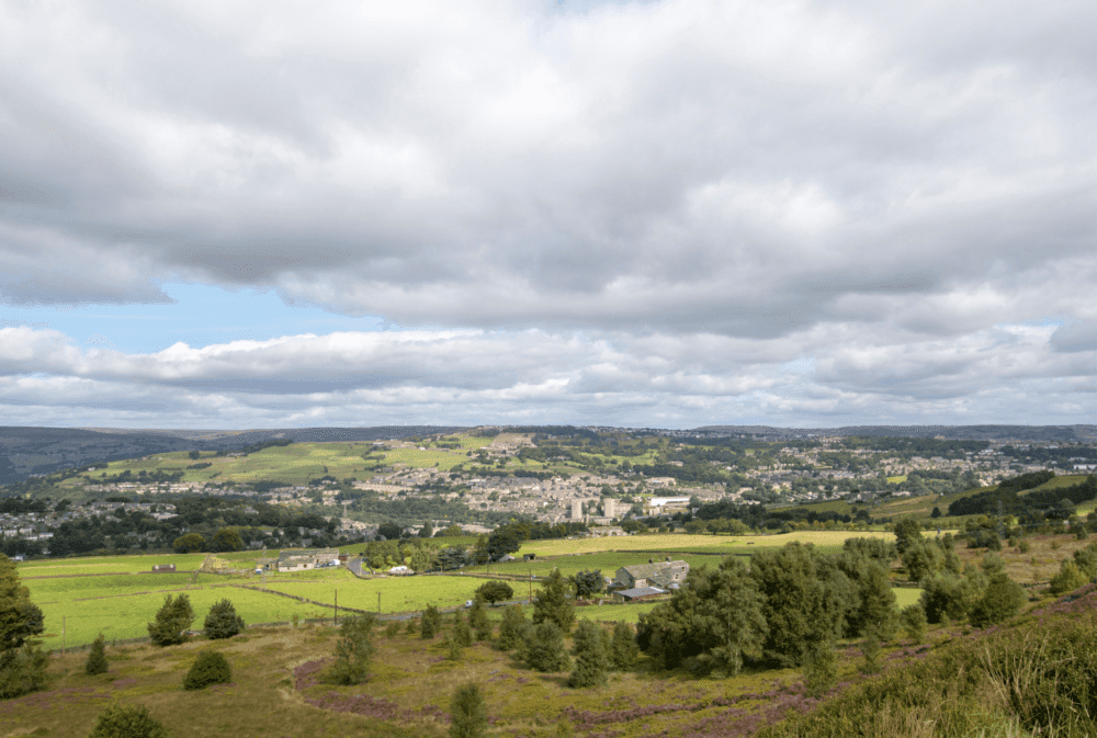 A scenic view of a countryside valley with green fields, scattered houses, and a cloudy sky overhead. - Home Instead