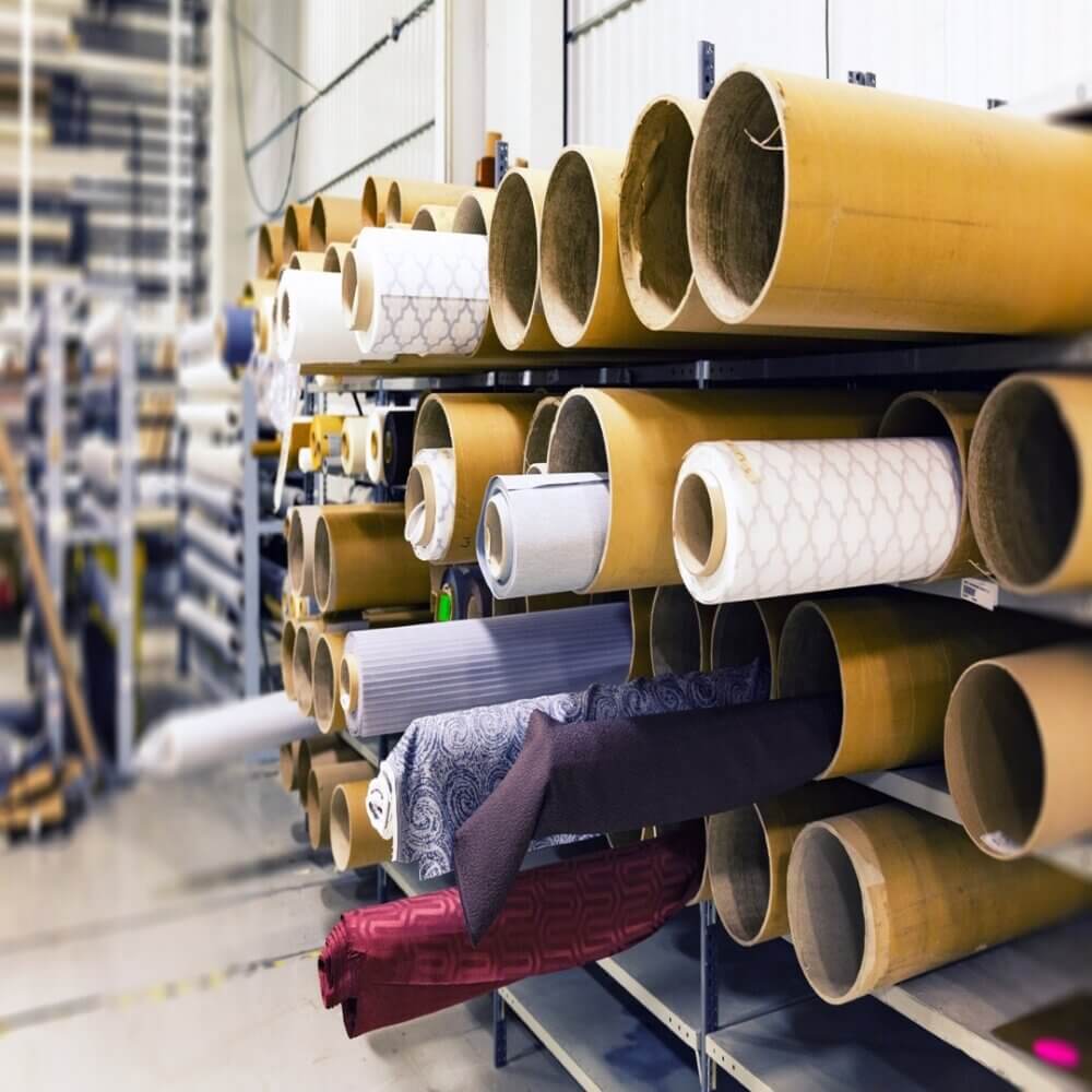 Rolls of various fabrics stored horizontally on shelves in a warehouse. - Home Instead