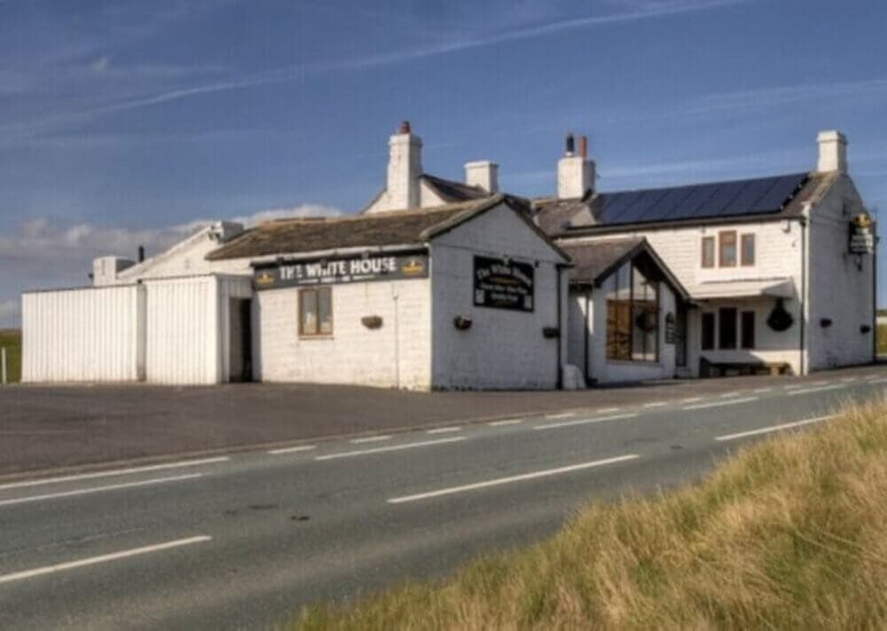 A white, rustic building by the roadside with signs reading "The White House" and solar panels on the roof. - Home Instead