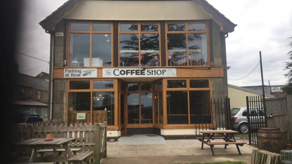 A two-story coffee shop with large windows, wooden outdoor seating, and a sign "COFFEE SHOP" above the entrance. - Home Instead