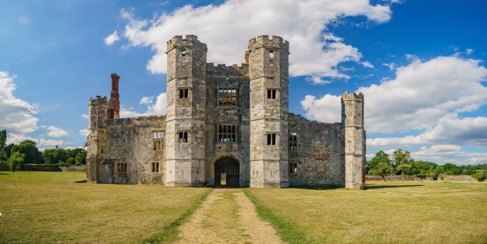 A historic stone castle with four round towers, set against a blue sky with clouds and surrounded by grass. - Home Instead