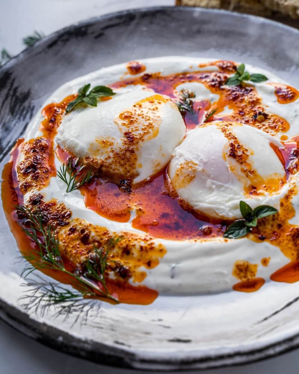 A plate of poached eggs on creamy yogurt, garnished with herbs and drizzled with a spiced oil sauce. - Home Instead
