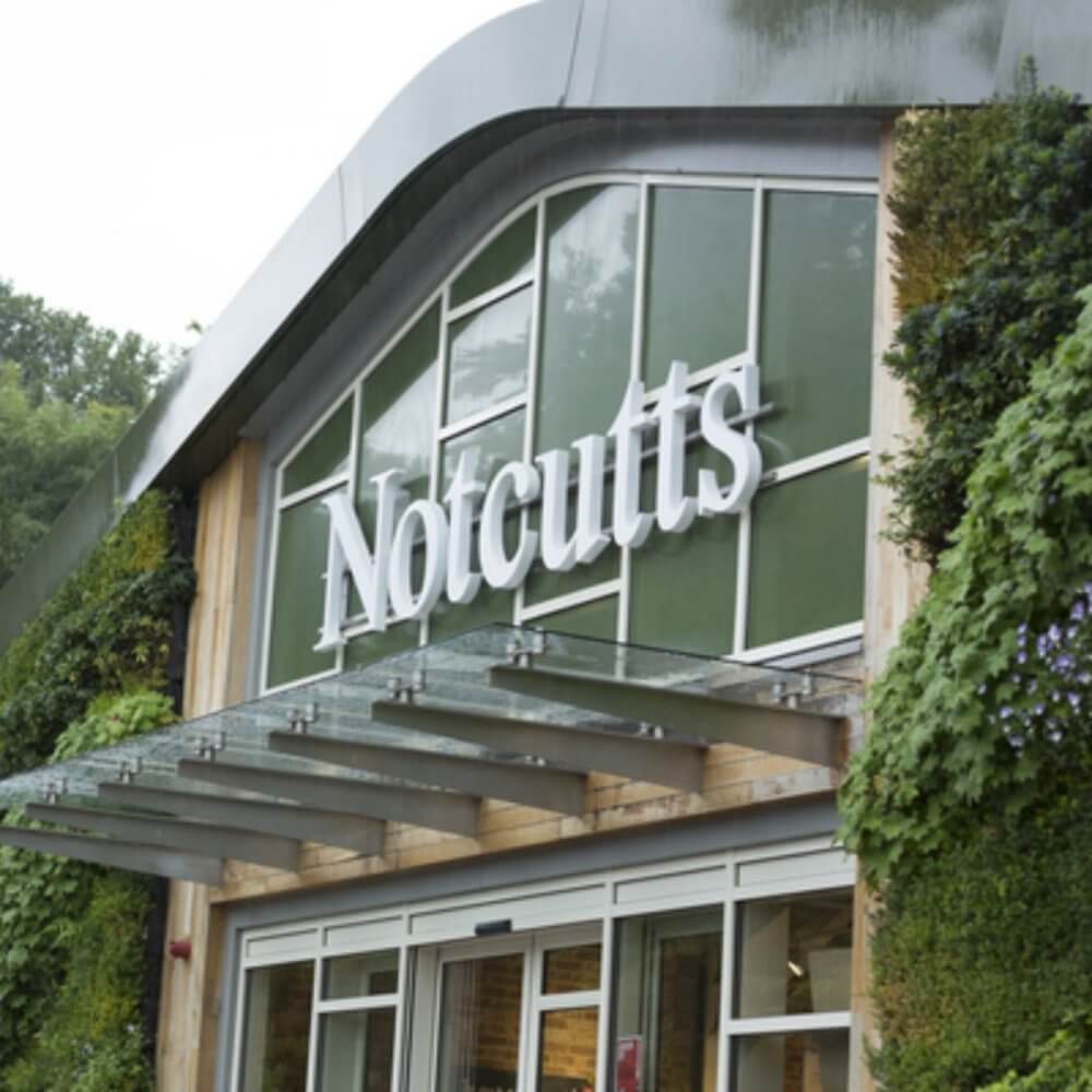 Entrance of Notcutts garden center with greenery around the building's glass facade. - Home Instead